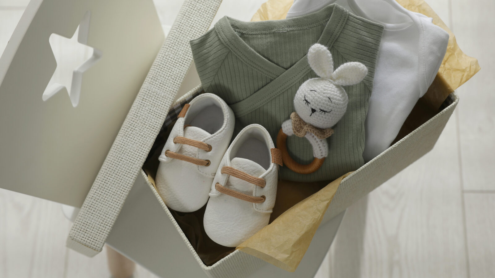 Box with baby clothes, shoes and toy on chair indoors, above vie